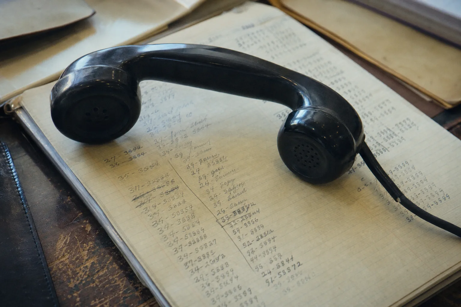 A telephone handset resting on a notepad covered in dated handwritten notes and reference numbers