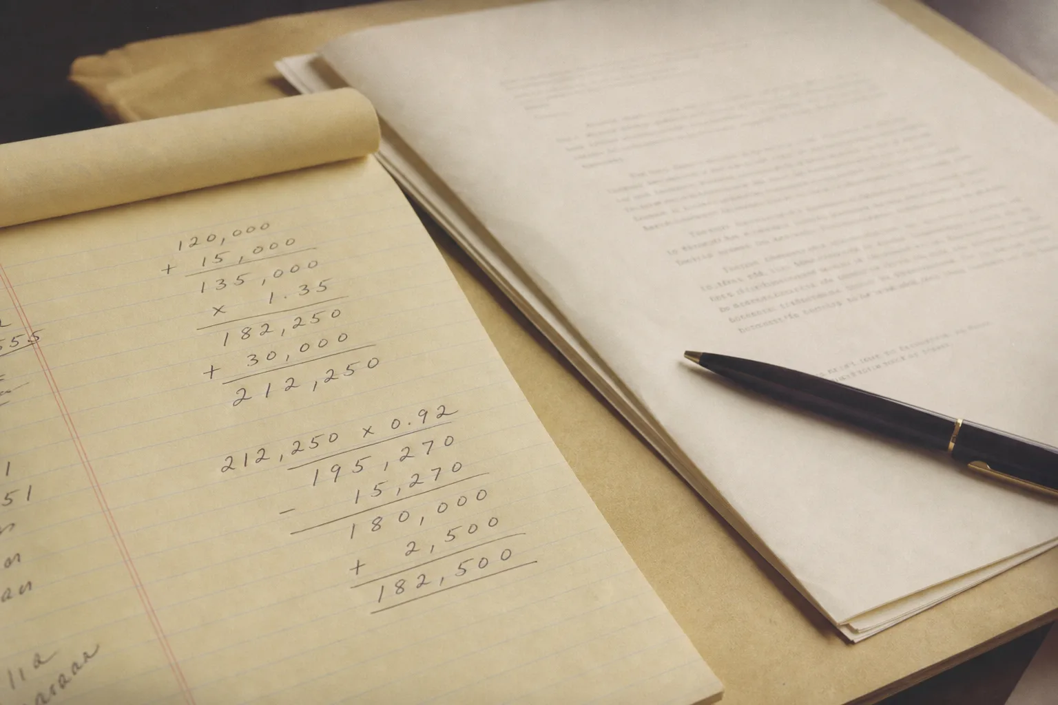 A notepad showing handwritten calculations beside a settlement letter and a pen