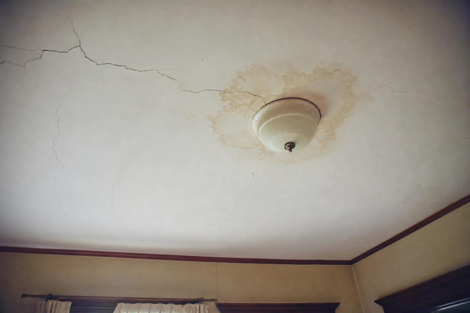 A cracked ceiling and a water stain around a light fixture in an older room