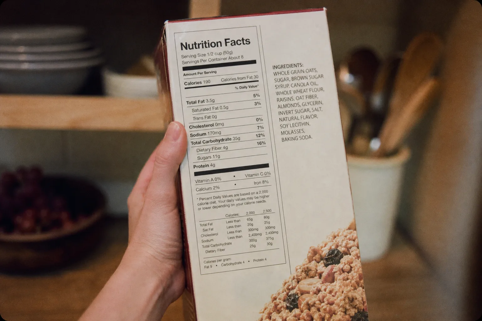 A nutrition facts panel and ingredient list on the back of a boxed food product, held up in a kitchen